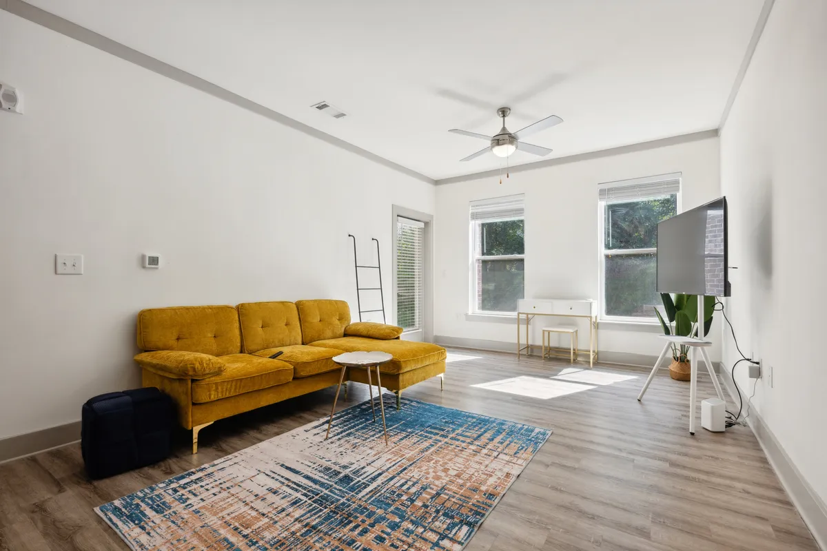 The image captures a stylish living area with a vibrant yellow couch as the centerpiece, a modern coffee table, a sleek TV setup, and a cozy rug, all bathed in cheerful natural light. The space invites relaxation and socializing, with a warm, modern vibe perfect for unwinding after a day of exploring Knoxville.