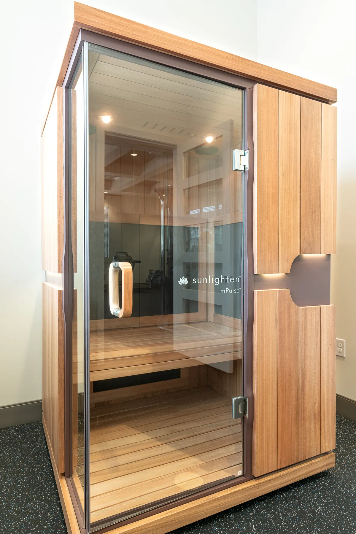 A tranquil wellness area showcasing an infrared sauna surrounded by smooth wooden panels and a glass door, designed for relaxation and self-care. The space is serene and invites rejuvenation after a busy day.