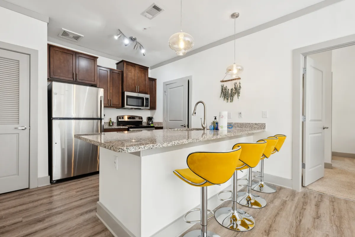 A vibrant view of the kitchen area, featuring a granite countertop, cheerful yellow bar stools, and stainless steel appliances. The setup is ideal for casual dining or entertaining guests, with an inviting and sociable atmosphere.