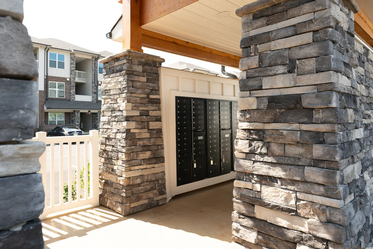 A community entrance scene with stone pillars, mailbox units, and stylish surrounding architecture, giving a first impression of the neighborhood and the lifestyle it offers. The area feels welcoming and hints at a vibrant community just outside the door.