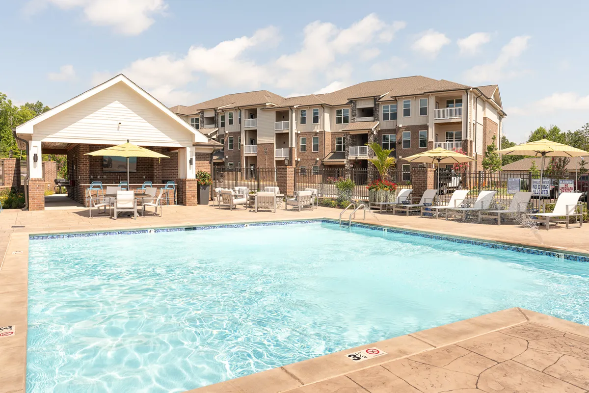 A welcoming outdoor pool area with lounge chairs, a covered seating area, and the apartment building in the background. The scene is set during sunset, with people relaxing and socializing, highlighting a sense of community and leisure.