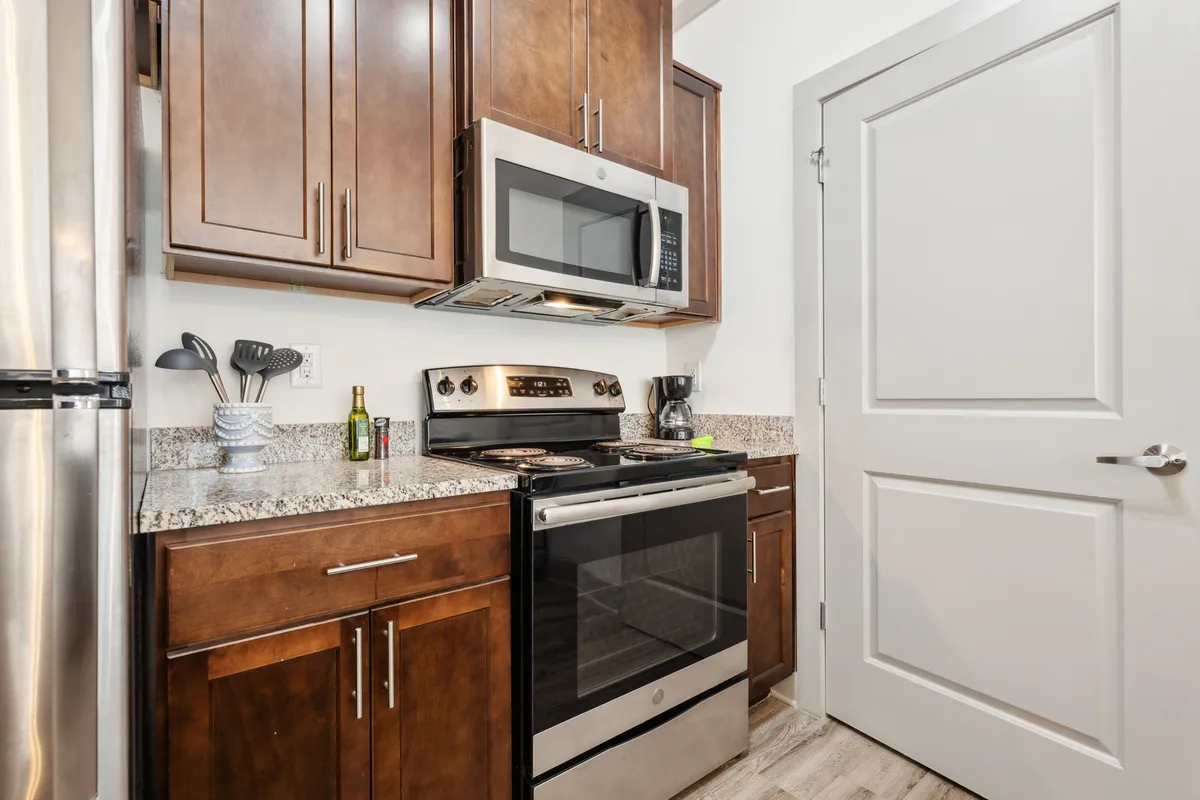 This image showcases a modern kitchen equipped with stainless steel appliances, granite countertops, and dark wood cabinets. The space exudes a contemporary and welcoming ambiance, with ample room for cooking and entertaining.
